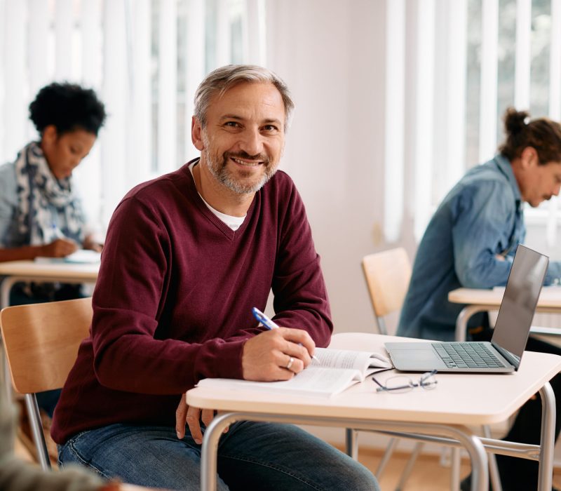 Happy mature man attending a lecture and writing notes while looking at camera.