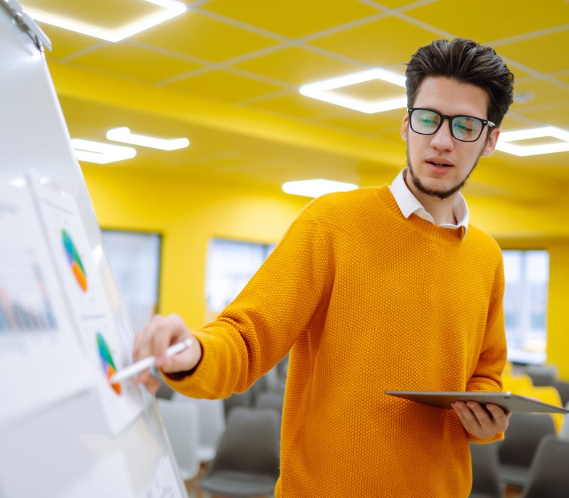 Young man  leader, presenter, make a business presentation at a conference in the office, business mentor explaining a graphic diagram on a flipchart, corporate group seminar.