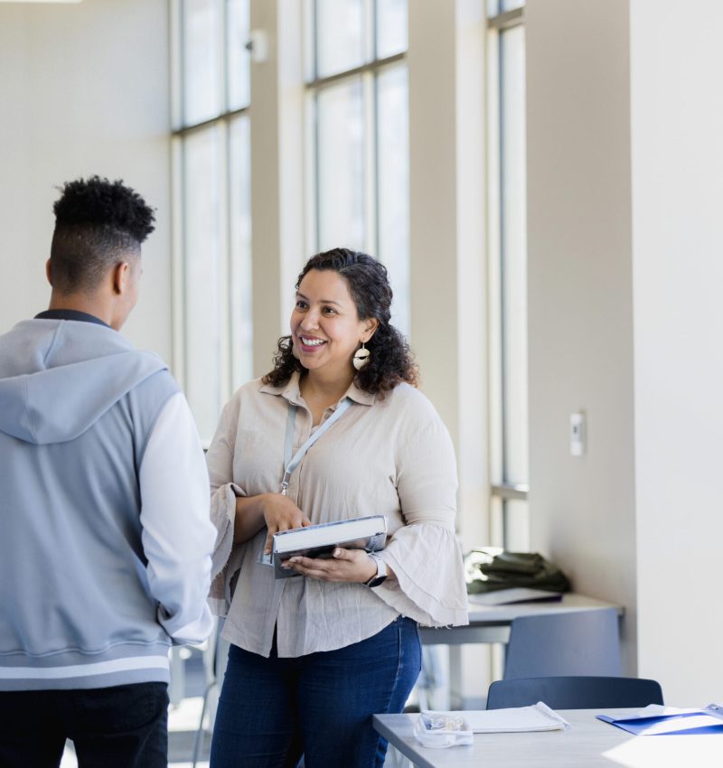 The librarian approaches the young adult man with a resource she found for his research paper.