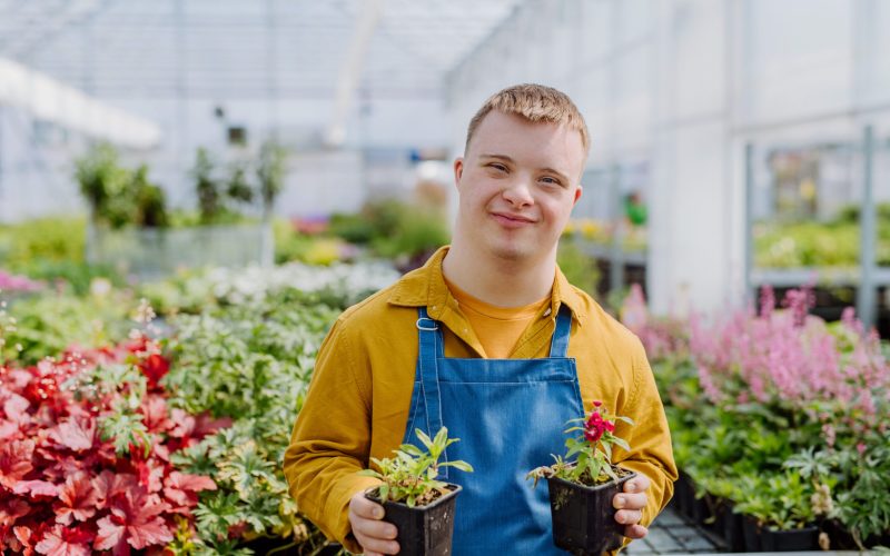 A happy young employee with Down syndrome working in garden centre, taking care of flowers.