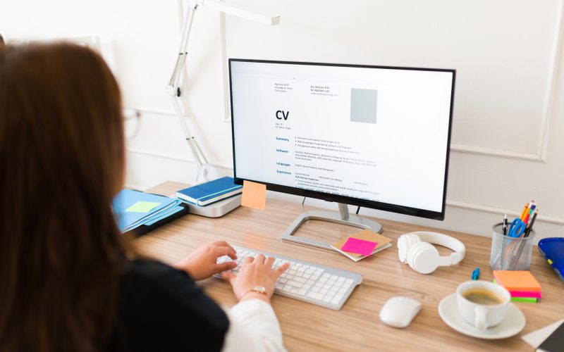 Professional woman seen from behind updating her curriculum or resume on the computer while applying for a new job