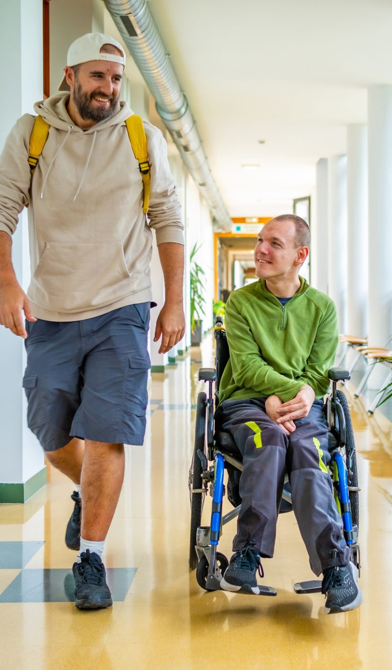 Man with physical disability in wheelchair and friend chatting distracted in the university